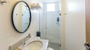 Une salle de bain moderne avec un grand miroir rond, un lavabo et une douche à parois de verre.