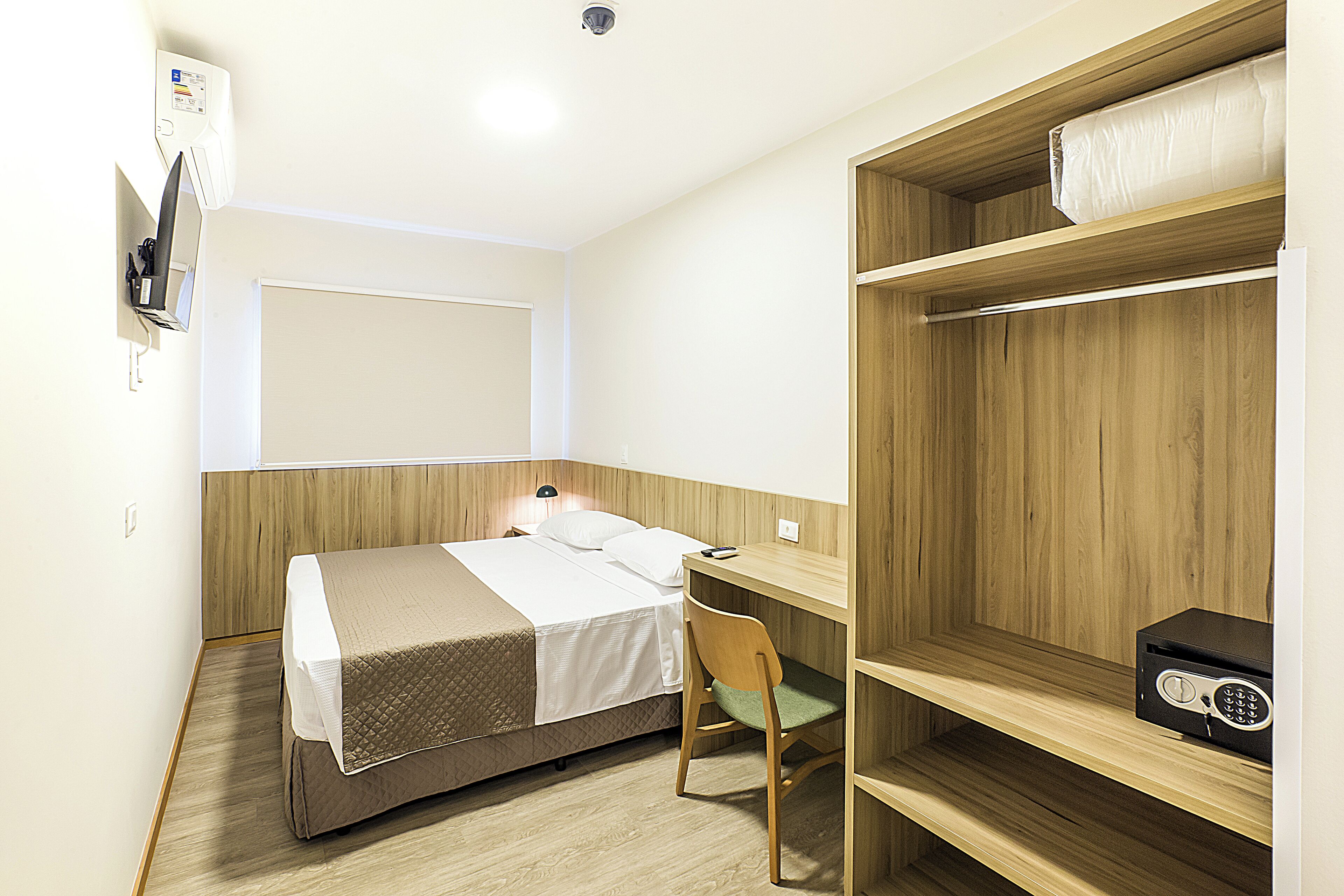 Een kleine hotelkamer met een bed, bureau, stoel en een plankje met een radio.