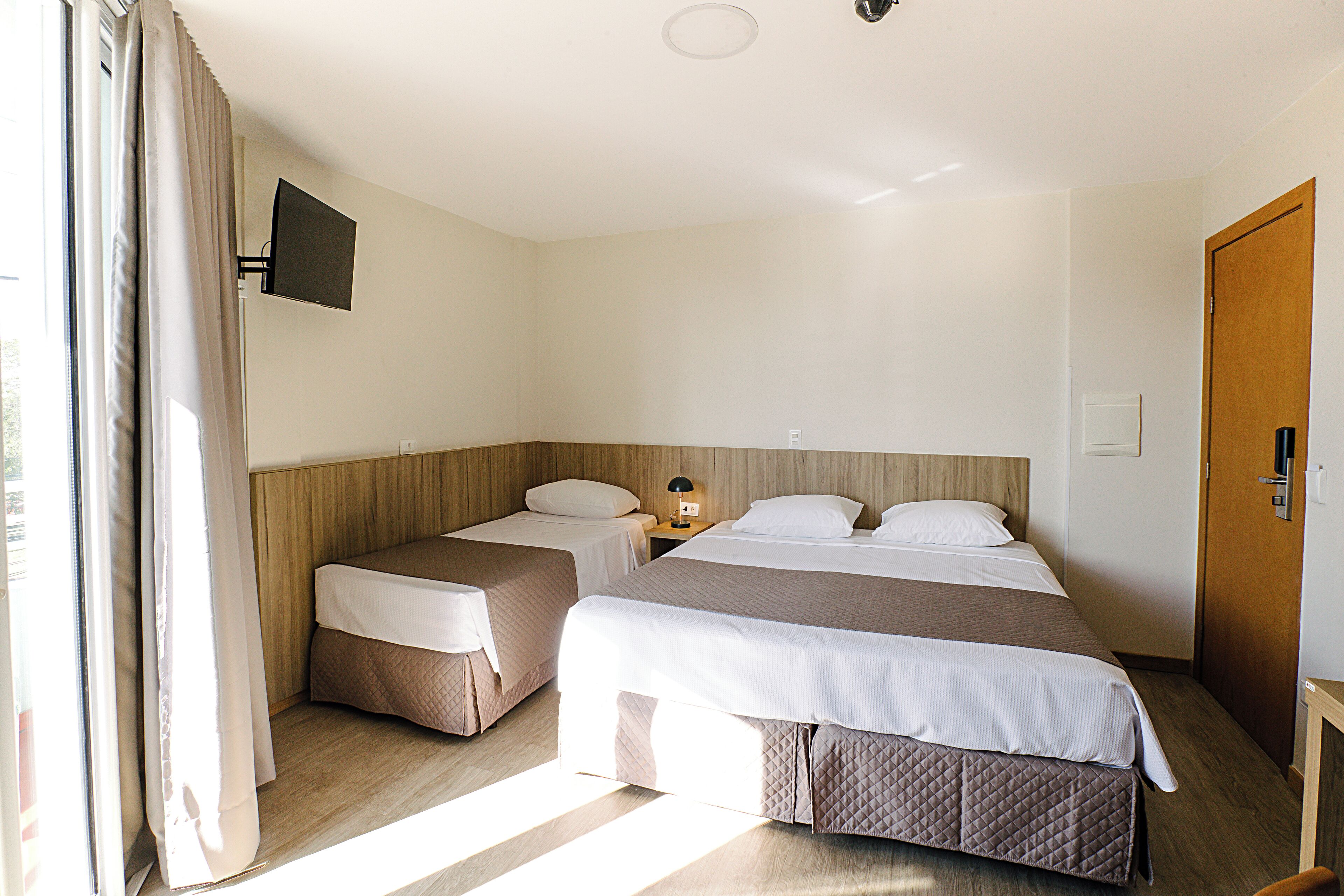 Ein Hotelzimmer mit zwei Betten, einem an der Wand befestigten Fernseher und einer Holztür.