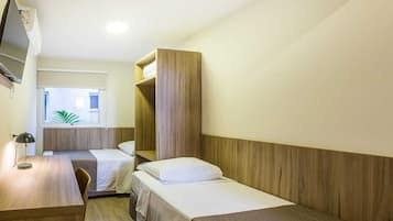 Een hotelkamer met twee enkele bedden, een houten hoofdbord, een bureau met lamp en een aan de muur bevestigde televisie.