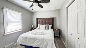 Une chambre à coucher avec un lit, un ventilateur de plafond, une table de chevet, une lampe et une porte.