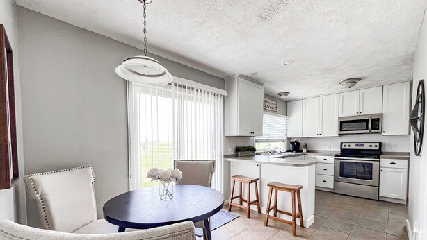 Une cuisine moderne avec des meubles blancs, un îlot central et un coin repas comprenant deux chaises et une table.