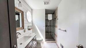 Une salle de bain moderne avec un meuble-lavabo blanc, une douche en verre et une lucarne visible.