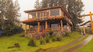 Una cabaña de madera rústica con balcón, rodeada de exuberante vegetación y un sendero de piedra.