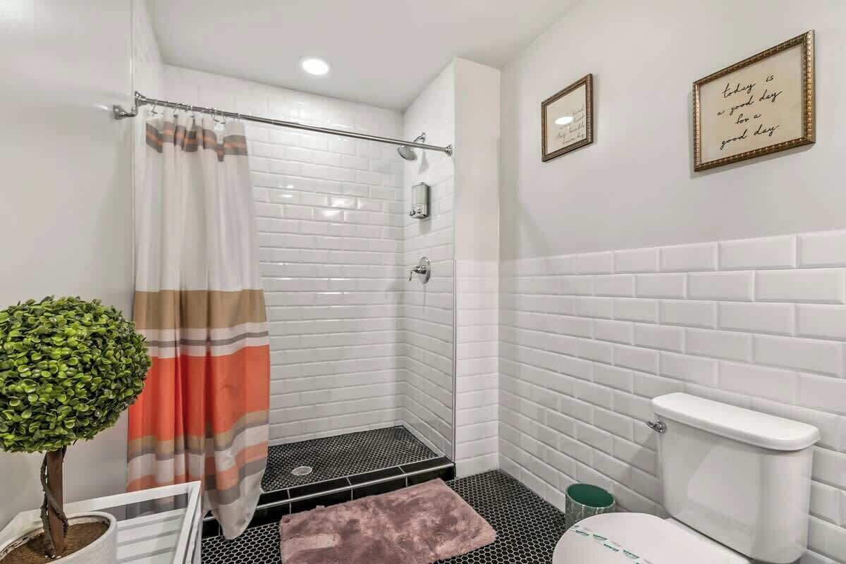 A modern bathroom with white subway tiles, a shower with a striped curtain, a small potted plant, and a toilet.