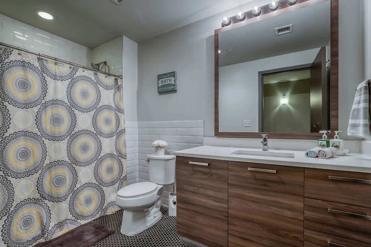 A bathroom with a shower curtain, toilet, sink, and mirror.