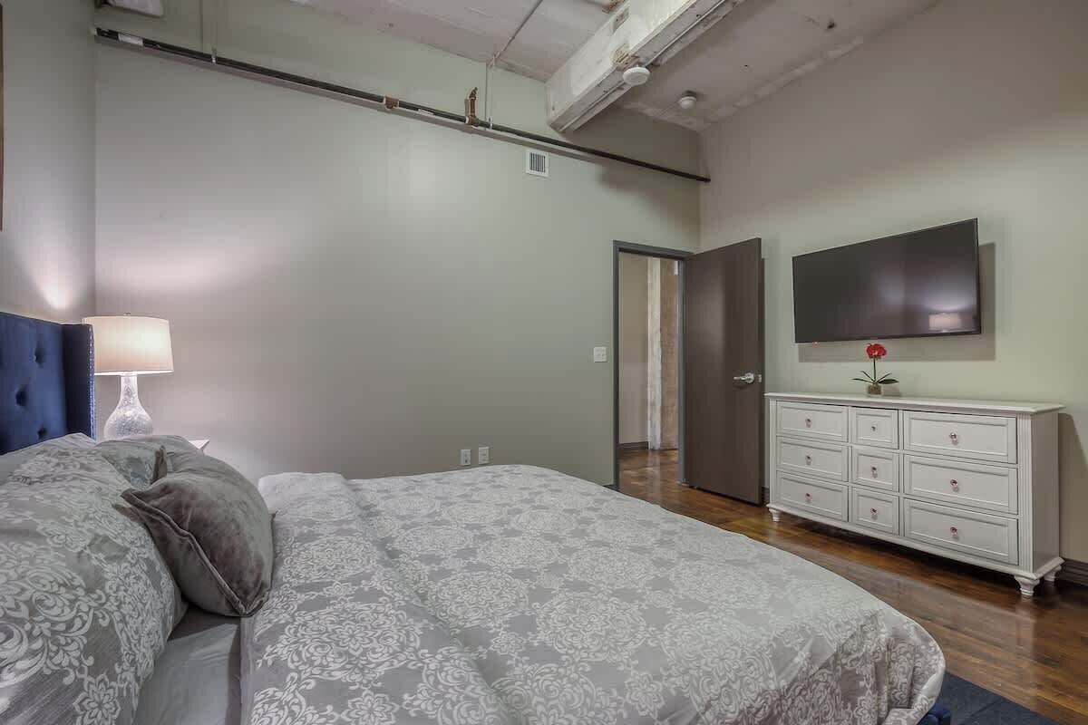 A bedroom with a bed, a dresser, a TV, and a door.