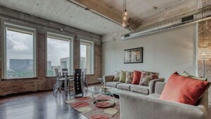 A spacious living room with large windows, a sofa, and a coffee table. - Resort-Style Loft w/ Free Valet (Dallas)