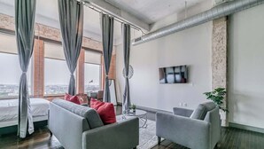 A modern living room with a grey sofa, two armchairs, a small round table, and a TV mounted on the wall. - Dallas Skyline Stay | Pool, Gym + Free Breakfast (Dallas)