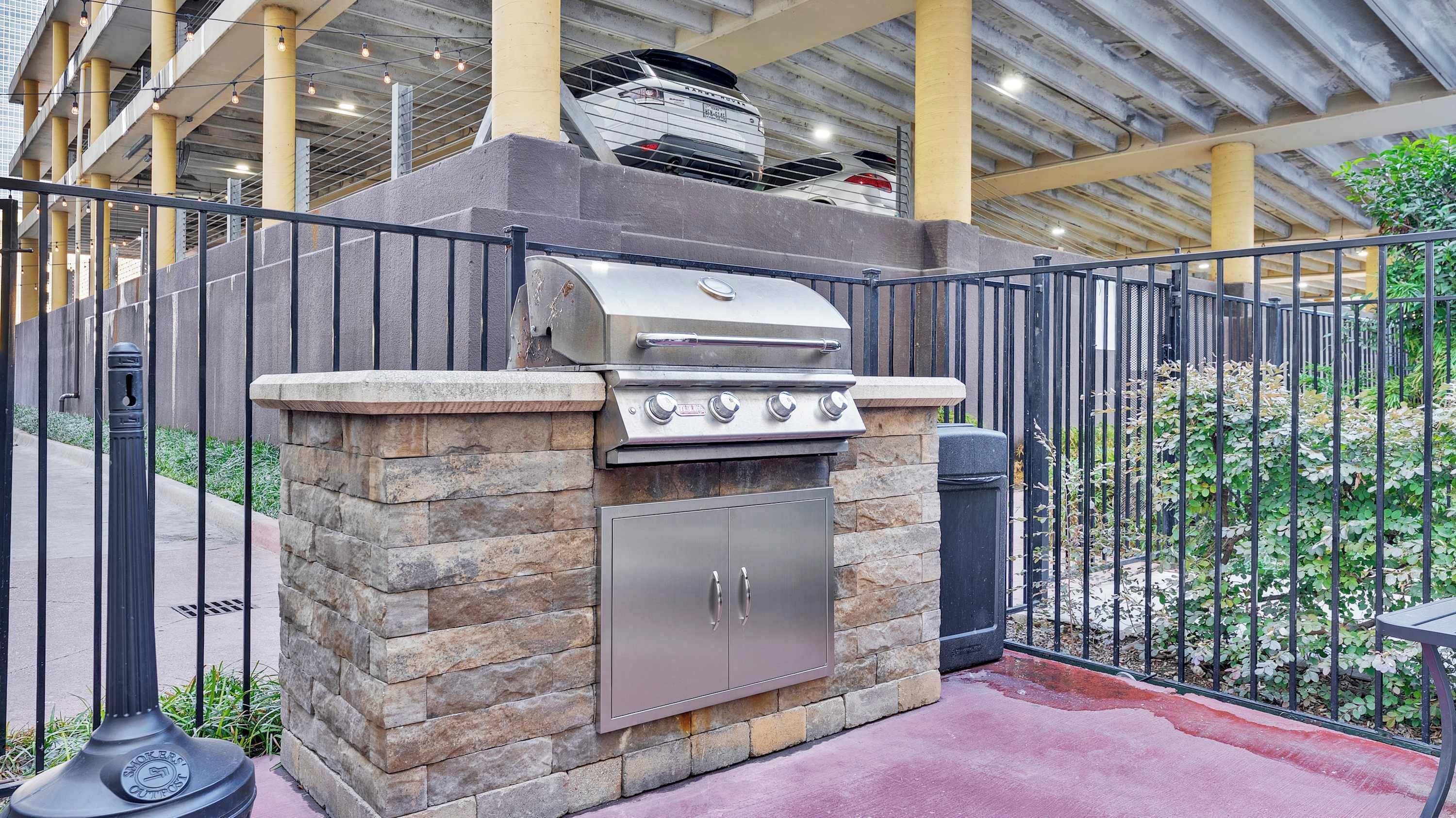 Un espace barbecue extérieur avec un mur en pierre, un barbecue en acier inoxydable et une poubelle.