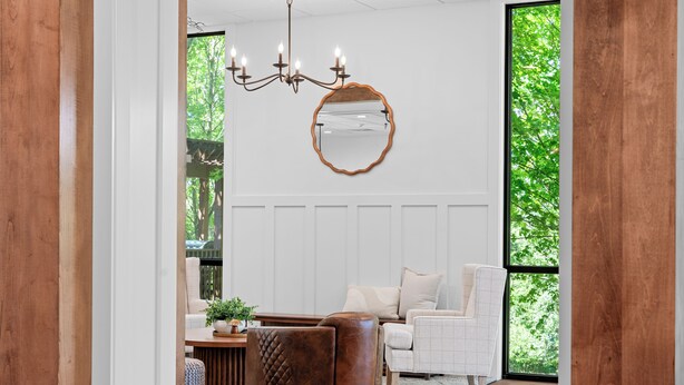 A modern living room with a large window, a chandelier, a round mirror, and a leather ottoman. - Branson Falls Lodge (Branson)