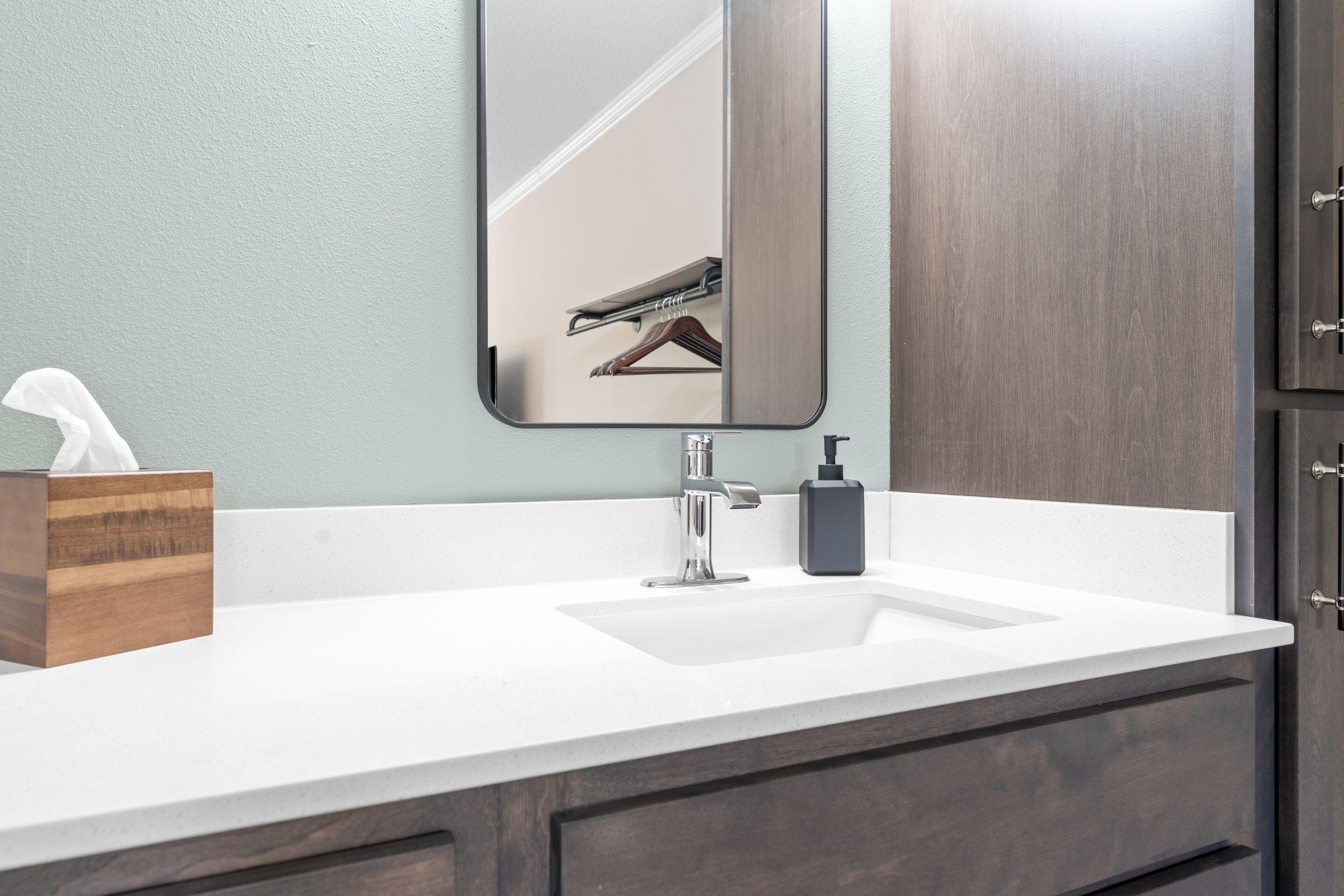 Une salle de bain avec un lavabo blanc, un miroir, un porte-mouchoirs en bois et un distributeur de savon.