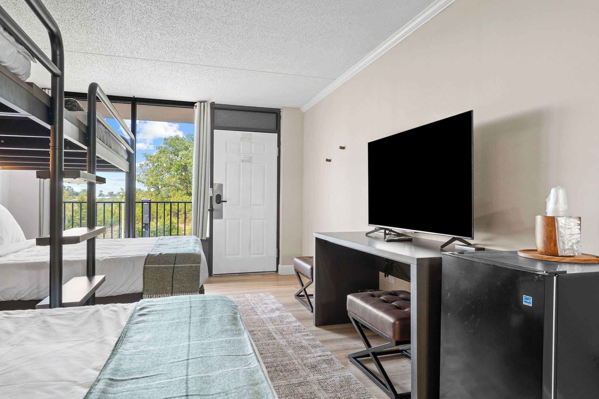 A modern room with bunk beds, a flat-screen TV, a refrigerator, and a view of the outdoors.