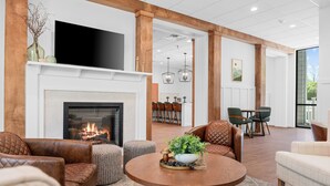 A spacious living area with a fireplace, leather sofas, a round wooden coffee table, and a television mounted above the fireplace. - Branson Falls Lodge (Branson)