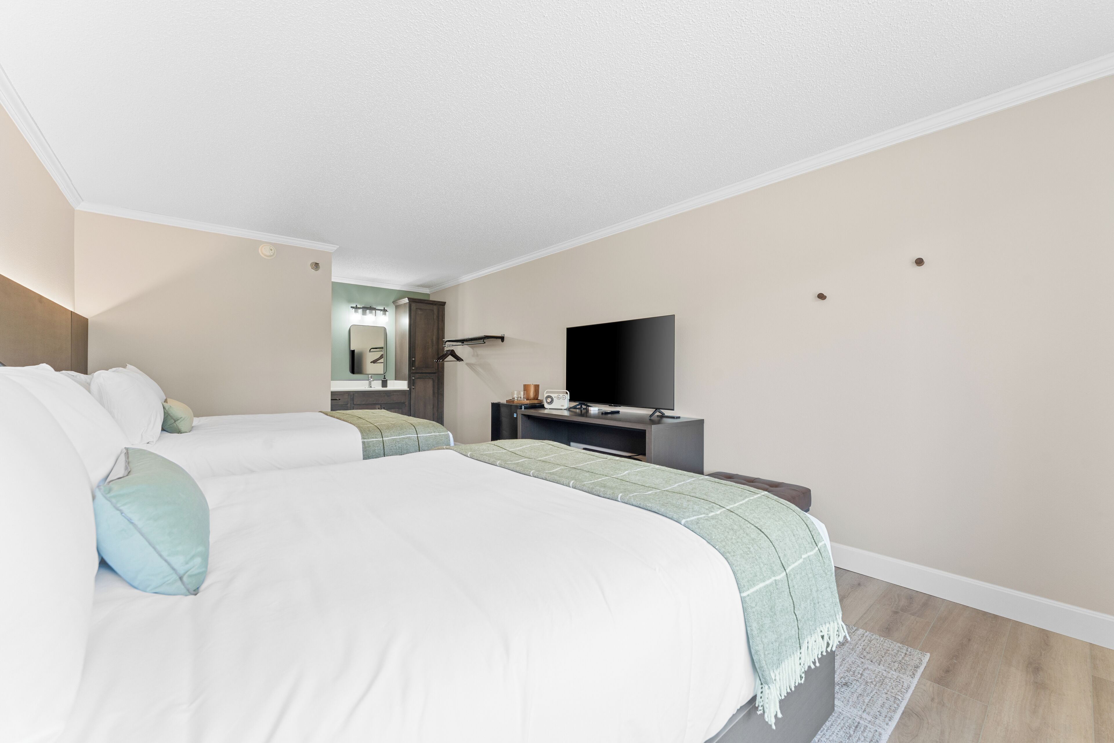 A hotel room with two beds, a flat-screen TV, a desk with a computer, and a mirror.