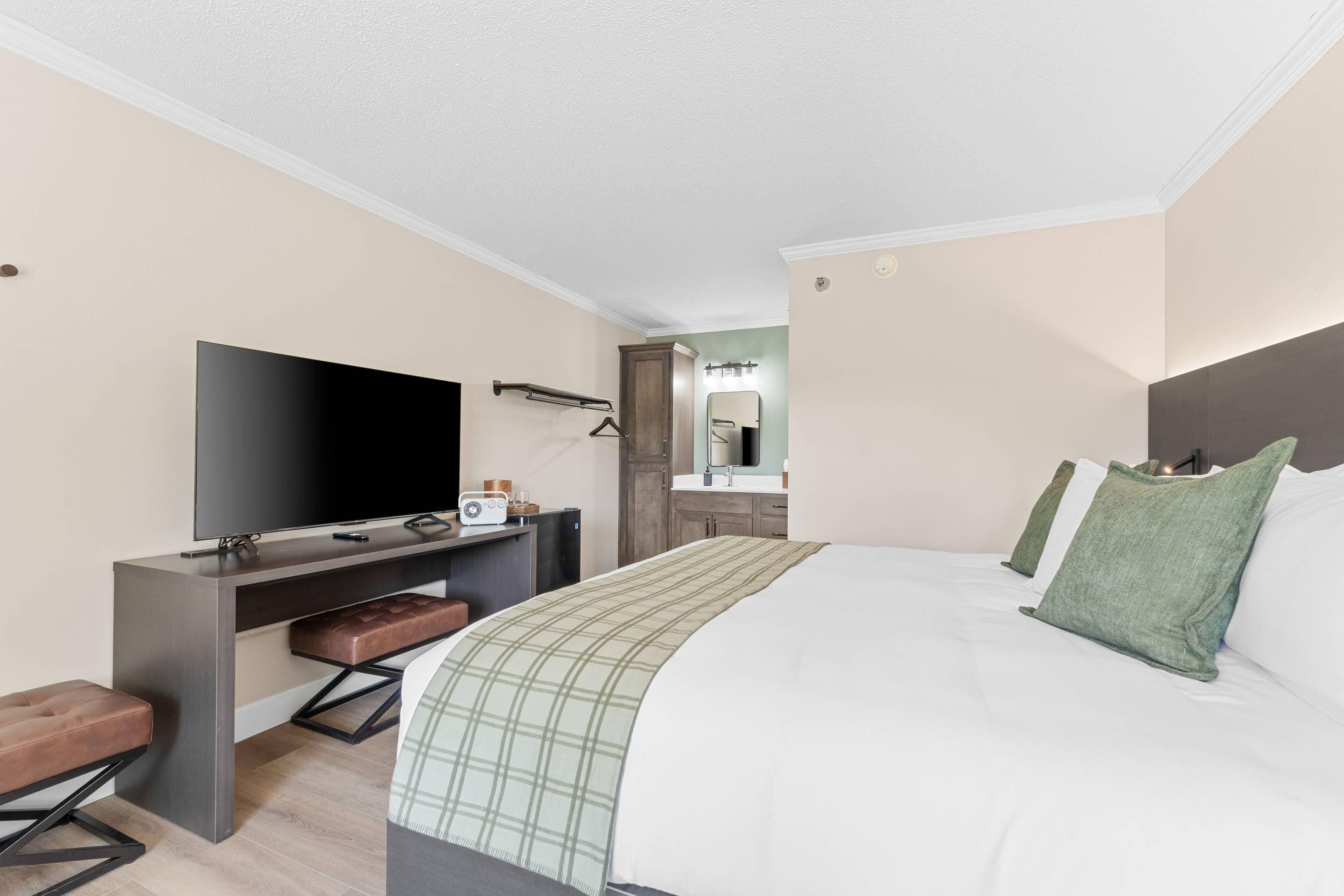 A hotel room with a bed, a desk with a flat-screen TV, a mirror, and a wardrobe.