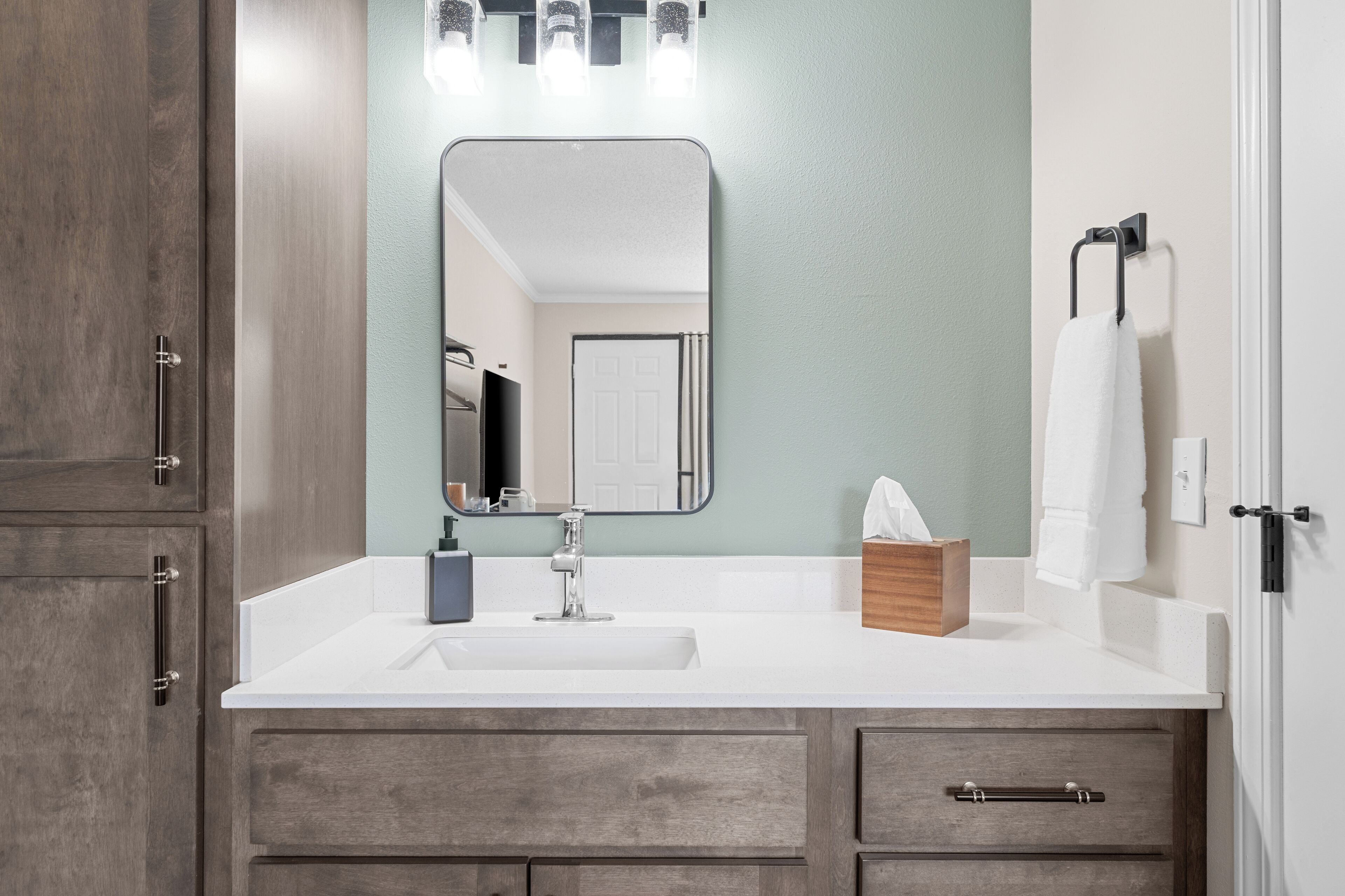 A bathroom with a white sink, wooden cabinets, a mirror, and a towel rack.