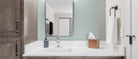 A bathroom with a white sink, wooden cabinets, a mirror, and a towel rack.