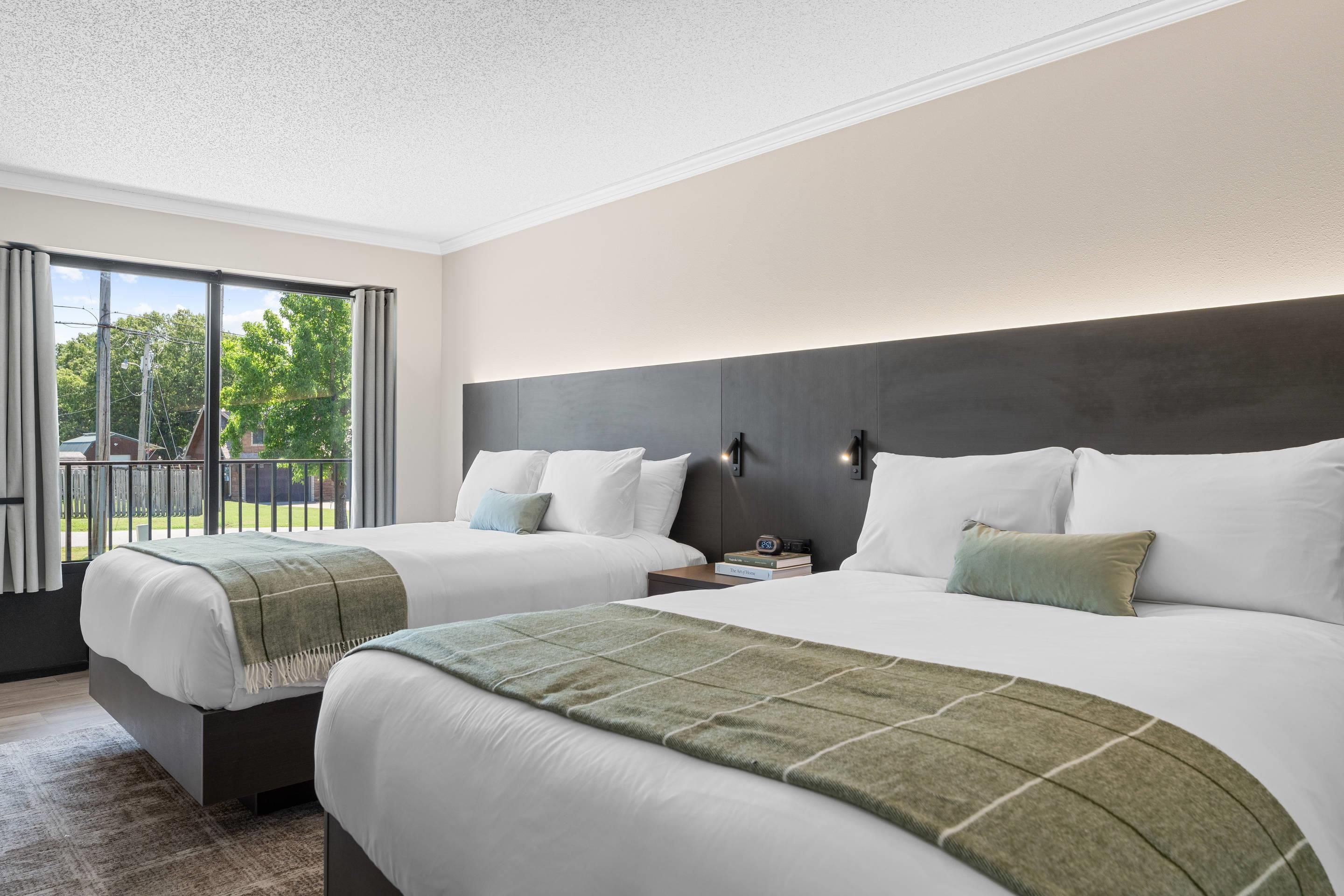 Een hotelkamer met twee bedden, een groot raam en uitzicht op groen.