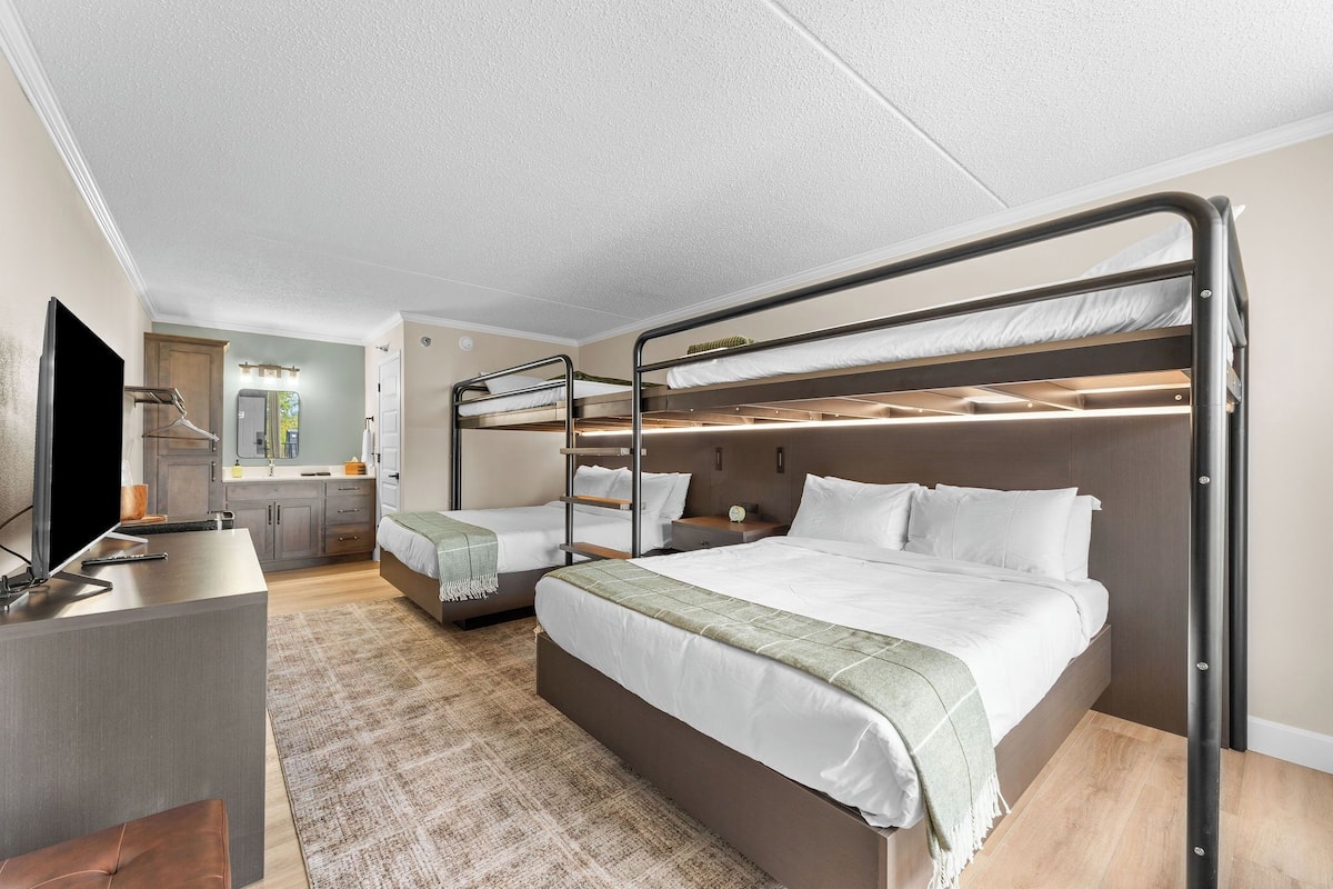 A modern hotel room with bunk beds, a desk, and a kitchenette.