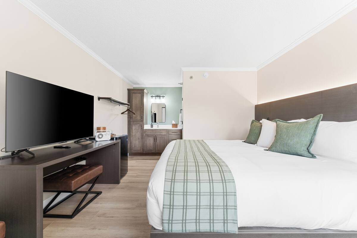 A hotel room with a bed, a TV, a desk, and a bathroom in the background.