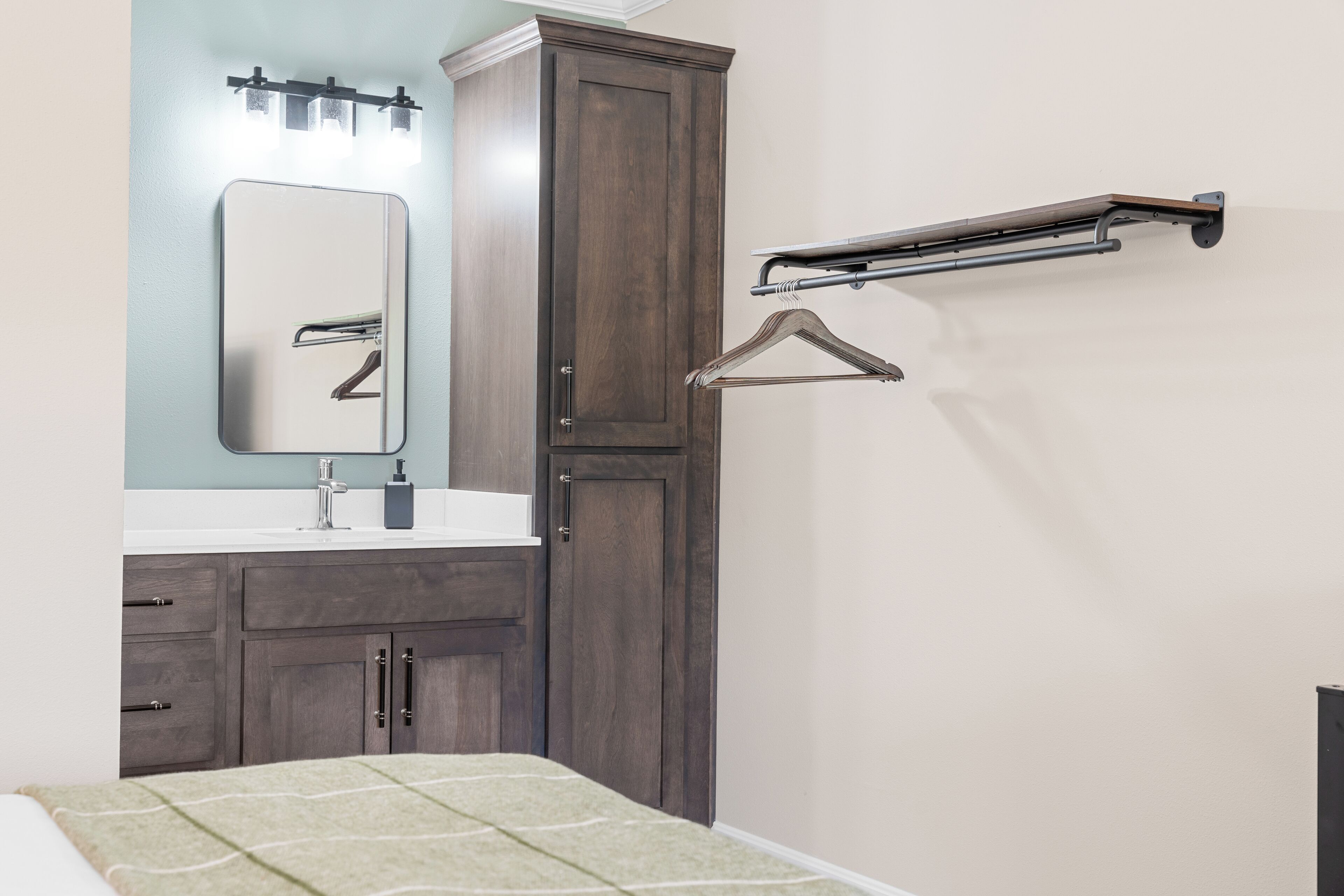 A bedroom with a bed, a dresser, a mirror, and a wall-mounted drying rack.