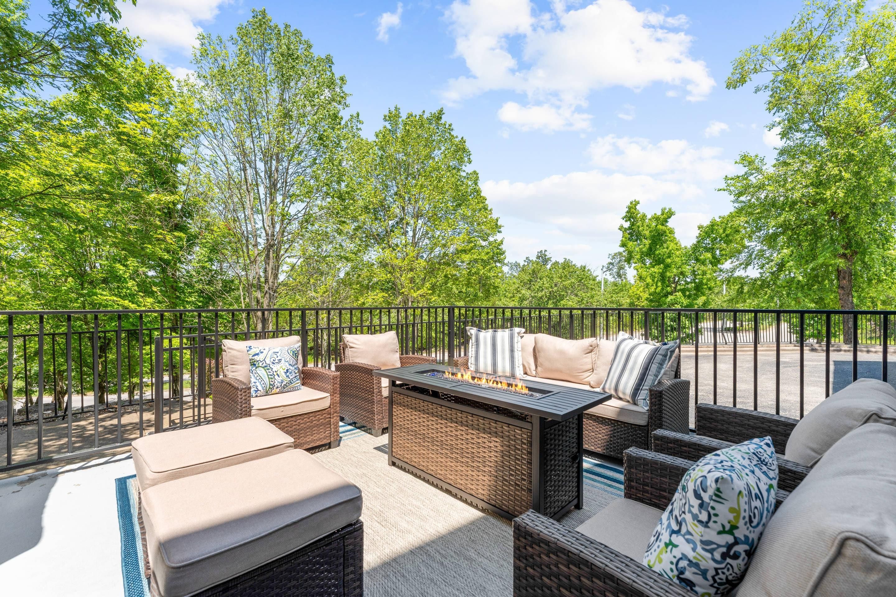 An outdoor patio with wicker furniture, a fire pit, and a view of trees and a road.