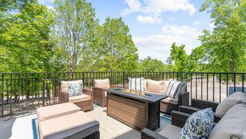 An outdoor patio with wicker furniture, a fire pit, and a view of trees and a road.