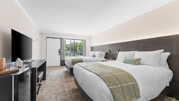 A modern hotel room with a large bed, a desk with a flat-screen TV, and a view of the outdoors through a sliding door.