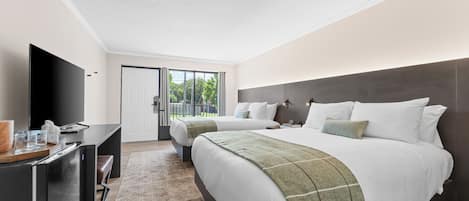A modern hotel room with a large bed, a desk with a flat-screen TV, and a view of the outdoors through a sliding door.