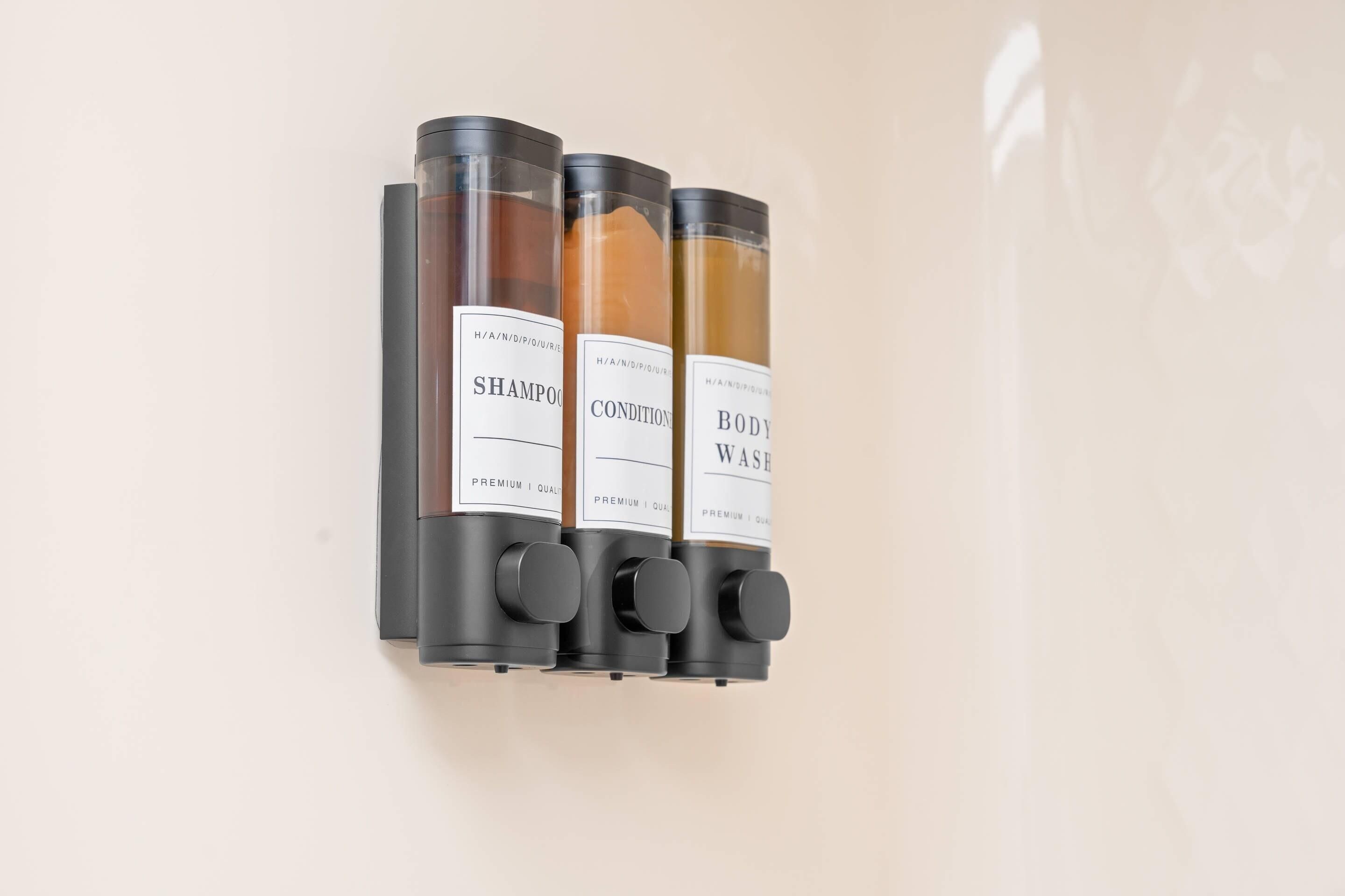 Tres botellas de champú y acondicionador sobre una pared.