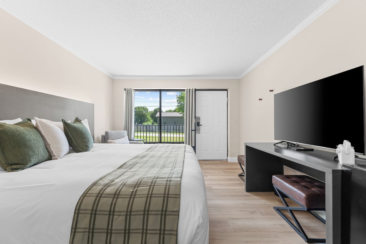 A hotel room with a bed, a desk, a television, and a sliding door to a balcony.