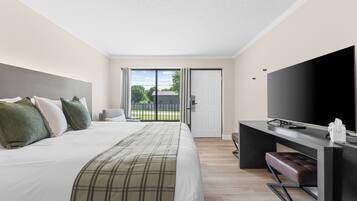 A hotel room with a bed, a desk, a television, and a sliding door to a balcony.