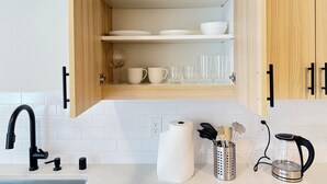 A kitchen with wooden cabinets, a black faucet, a roll of paper towels, and a kettle on the counter. - The Willow Stay (Vancouver)