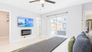 Een moderne woonkamer met een flatscreen televisie, een open haard, een plafondventilator en uitzicht door glazen deuren op een buitenruimte.
