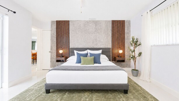 Een moderne slaapkamer met een groot bed, twee nachtkastjes met lampen, een potplant en uitzicht op een eetgedeelte.