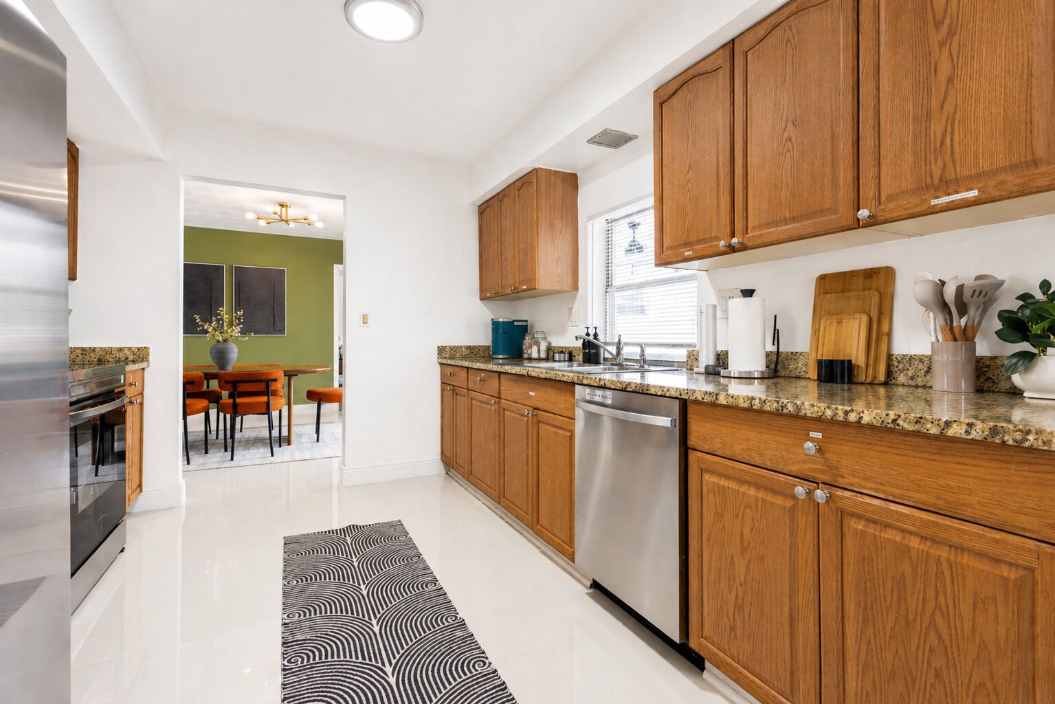 Una cocina moderna con armarios de madera, electrodomésticos de acero inoxidable y un comedor con sillas color naranja.