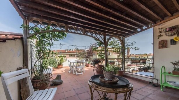 Eine überdachte Terrasse mit Tisch und Stühlen, Blumentöpfen und Blick auf die Stadtlandschaft.