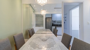 Un coin repas avec une table dressée pour quatre personnes, un lustre et une cuisine en arrière-plan.