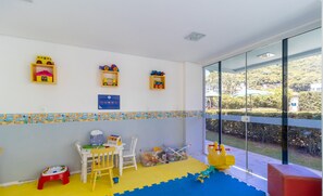 Een kinderspeelruimte met speelgoed, een kleintje tafel, stoelen en een kleed.