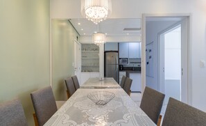 Een eetruimte met een tafel voor vier personen, een kroonluchter en een keuken op de achtergrond.