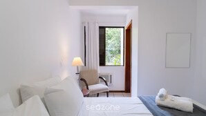 A hotel room with a bed, a chair, a lamp, a window with curtains, and a towel on the bed. - Apt 300m From the Charming Praia Brava Ccu203 (Florianópolis)