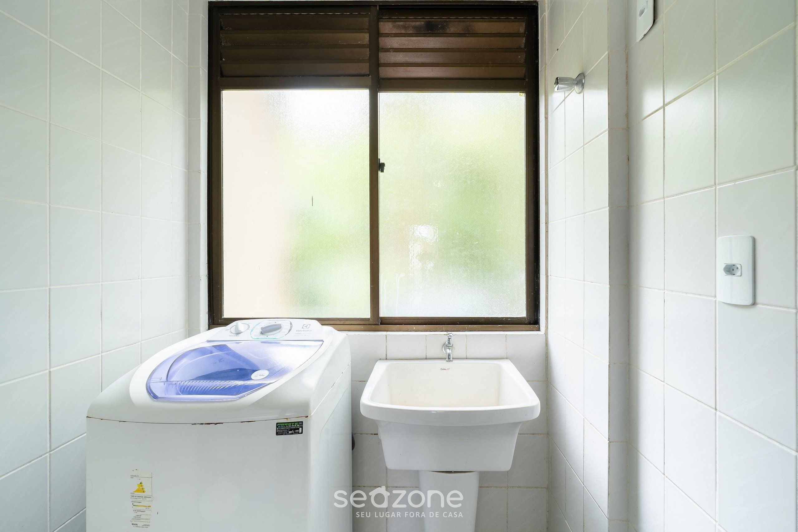 Un baño pequeño con lavadora, lavamanos y ventana con persianas.