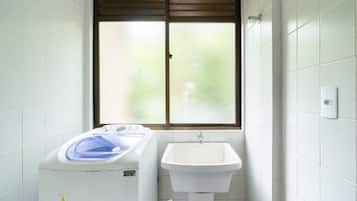Un baño pequeño con lavadora, lavamanos y ventana con persianas.