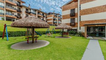 A playground with swings and a slide, surrounded by a well-maintained lawn and a building with multiple balconies.