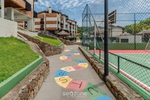 Un chemin bordé de lettres colorées qui mène à un court de tennis, entouré de bâtiments et d’une zone herbeuse.
