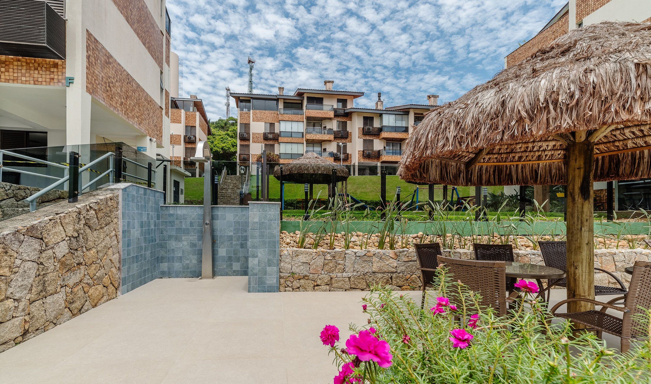 Um resort com um caminho de pedra que leva a um gazebo com telhado de palha, cercado por assentos externos e flores vibrantes.