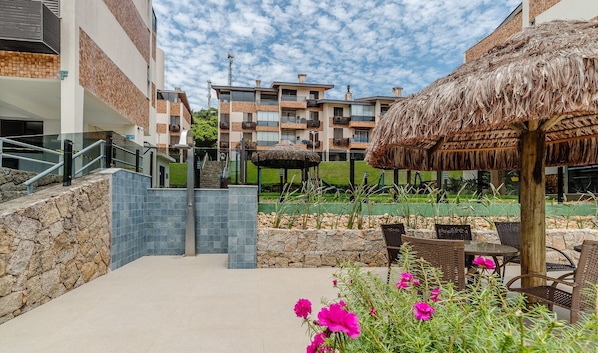 A resort with a stone pathway leading to a thatched-roof gazebo, surrounded by outdoor seating and vibrant flowers.