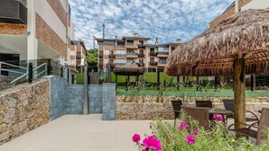 A resort with a stone pathway leading to a thatched-roof gazebo, surrounded by outdoor seating and vibrant flowers. - Apt 300m From the Charming Praia Brava Ccu203 (Florianópolis)