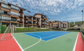 Un court de tennis avec un filet, entouré d’immeubles à plusieurs étages dotés de balcons.